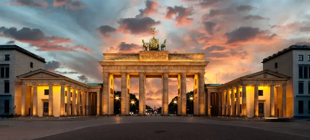 Brandenburg Gate illuminated at sunset with dramatic orange sky showcasing Berlin's iconic neoclassical architecture