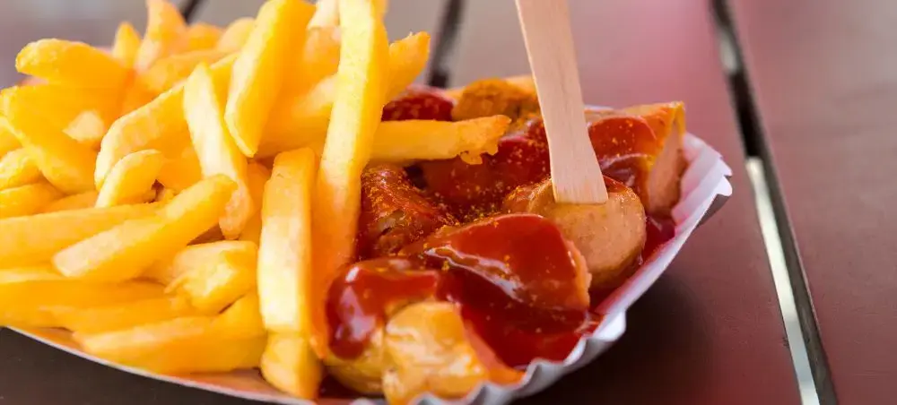 Traditional German currywurst with golden fries served in paper tray, showcasing Berlin's iconic street food culture