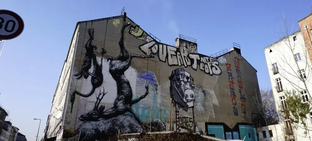 Large street art mural featuring dark silhouettes and graffiti on Berlin building wall under blue sky