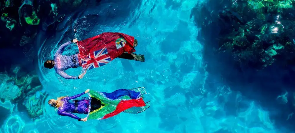 Aerial view of two swimmers floating in crystal-clear turquoise waters off Bermuda's pristine coastline