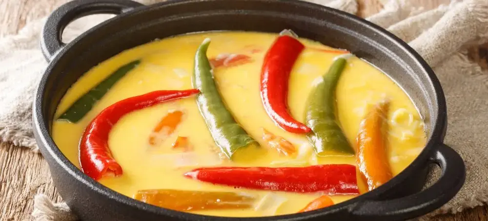 Traditional Bhutanese ema datshi curry with chilies and yak cheese in cast iron pot on wooden table