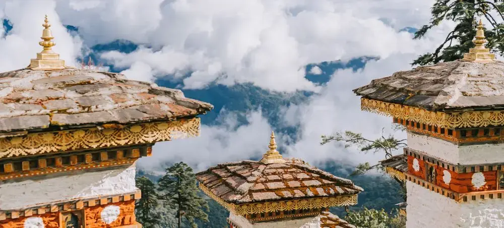 Traditional Bhutanese temple architecture with ornate golden details set against misty Himalayan mountains