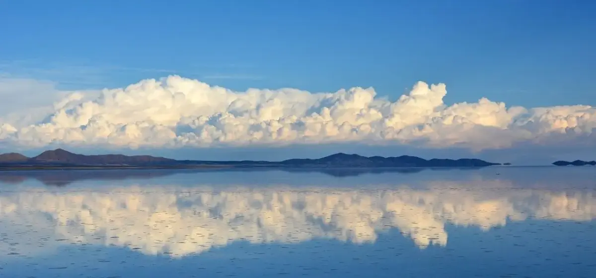 Stunning mirror-like reflection of dramatic clouds over Bolivia's pristine salt flats with distant mountains