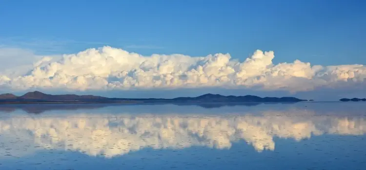 Serene Bolivian salt flats reflecting dramatic clouds and distant mountains under expansive blue sky