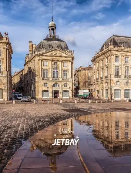 Historic Place de la Bourse in Bordeaux reflecting in wet cobblestones under dramatic blue sky