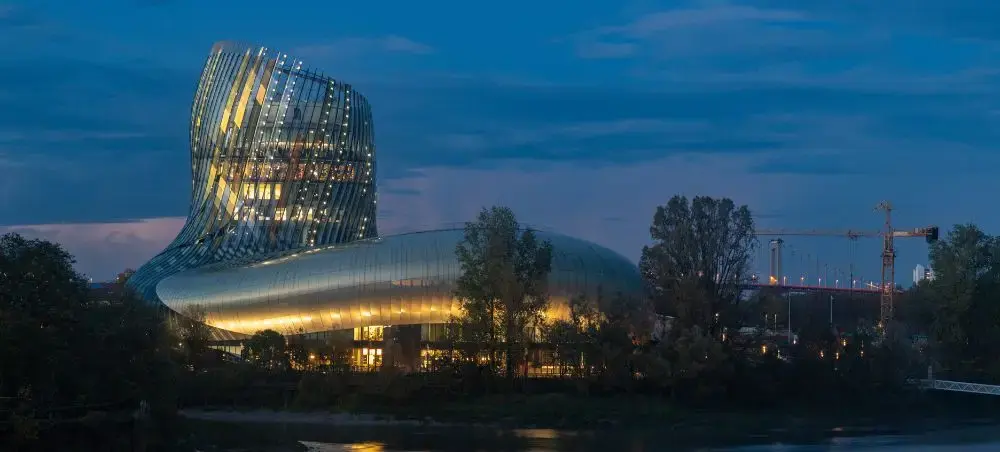 Modern Bordeaux wine museum with illuminated curved architecture reflecting in river at dusk