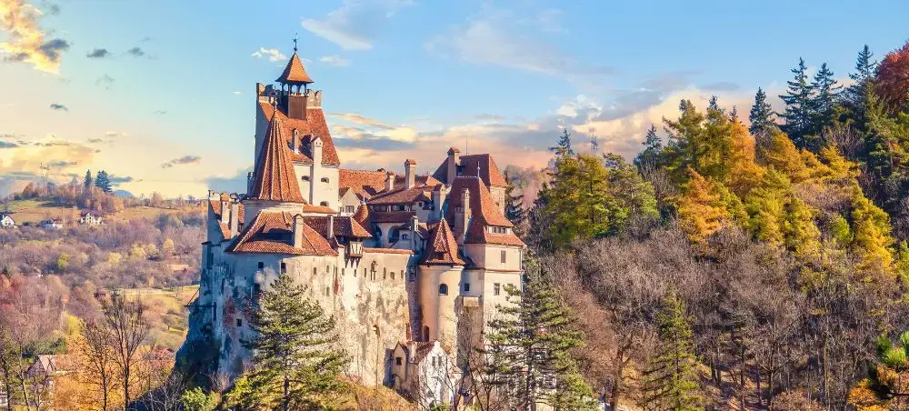 Bran Castle perched dramatically on a rocky cliff surrounded by autumn foliage in Brasov, Romania