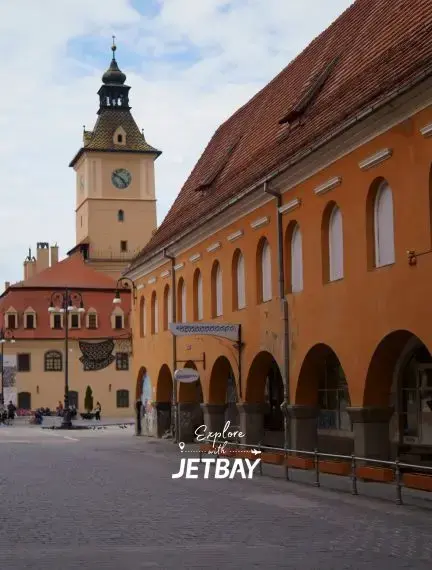 Historic clock tower and colorful baroque buildings surrounding Brasov's cobblestone main square in Romania