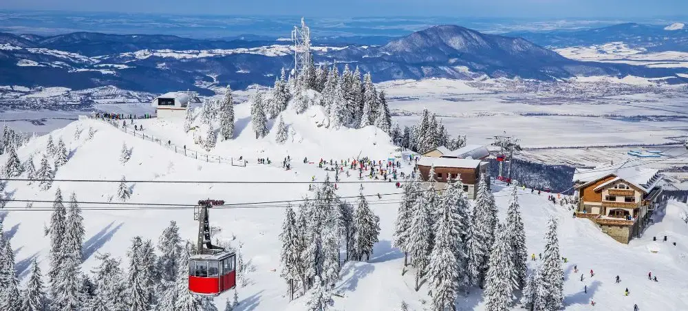 Aerial view of Brasov ski resort with red cable car, snow-covered slopes, and mountain chalets in Romania
