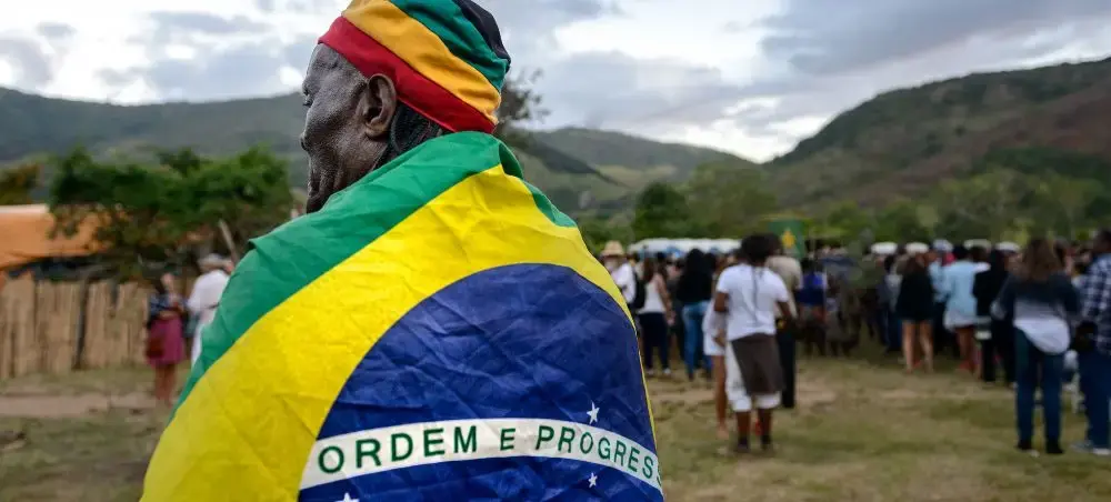 Brazilian man wearing national flag as cape celebrates at outdoor cultural festival in mountainous region