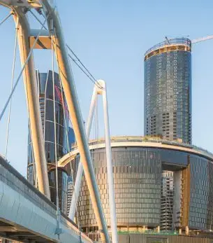 Golden suspension bridge cables frame Brisbane's modern skyline and towering skyscrapers at sunset