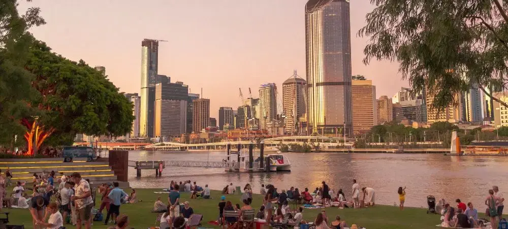 Brisbane skyline at sunset with crowds enjoying riverside parkland and luxury boats on the Brisbane River
