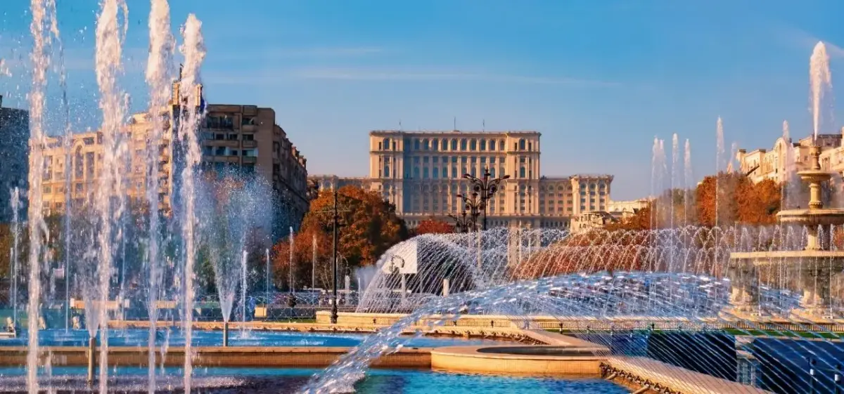 Spectacular fountain display in central Bucharest with Parliament Palace and autumn foliage under golden hour sky
