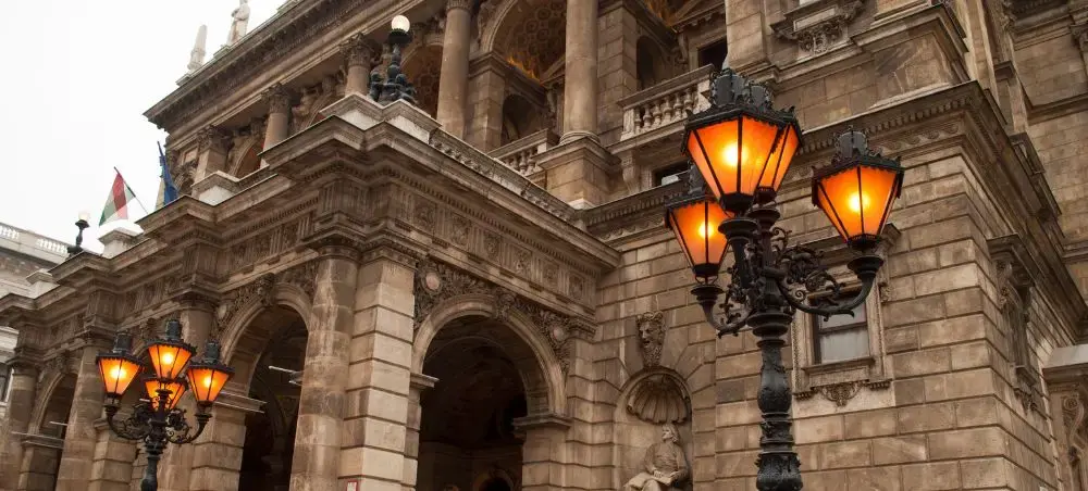 Historic Hungarian opera house facade with ornate columns and glowing street lamps at twilight