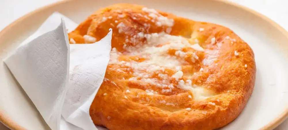 Golden Hungarian lángos flatbread with sour cream served on ceramic plate, traditional Budapest street food