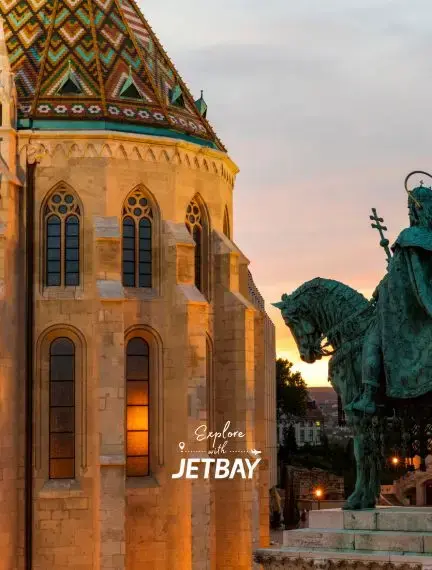 Historic Matthias Church with colorful tiled roof and bronze statue at sunset in Budapest, Hungary