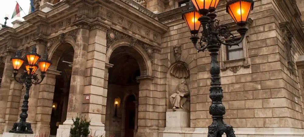 Historic Budapest Opera House facade with ornate stone architecture and glowing street lamps at dusk