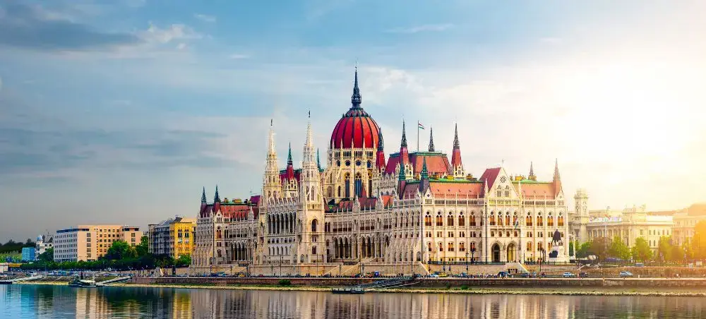 Hungarian Parliament Building's iconic red dome and Gothic Revival architecture reflected in Danube River at sunset