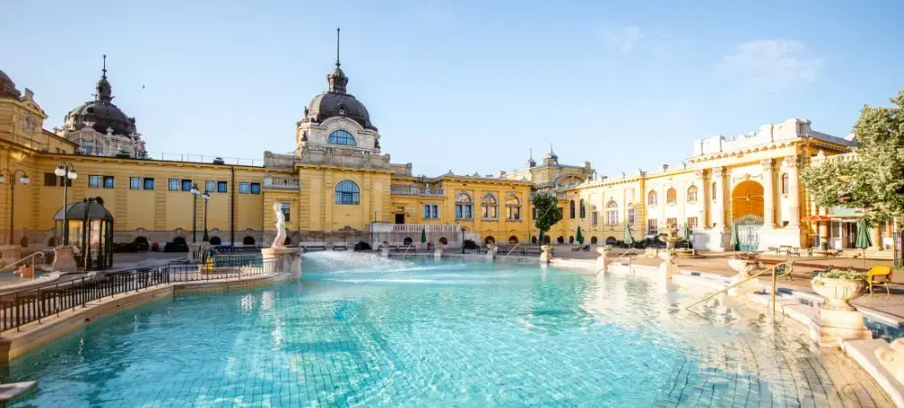 Széchenyi Thermal Baths in Budapest featuring ornate yellow baroque architecture and steaming outdoor pools