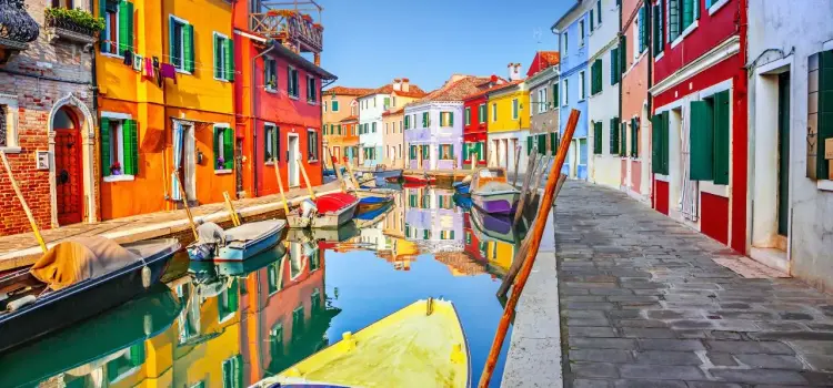 Vibrant rainbow-colored houses line a peaceful canal in Burano, Italy with traditional fishing boats