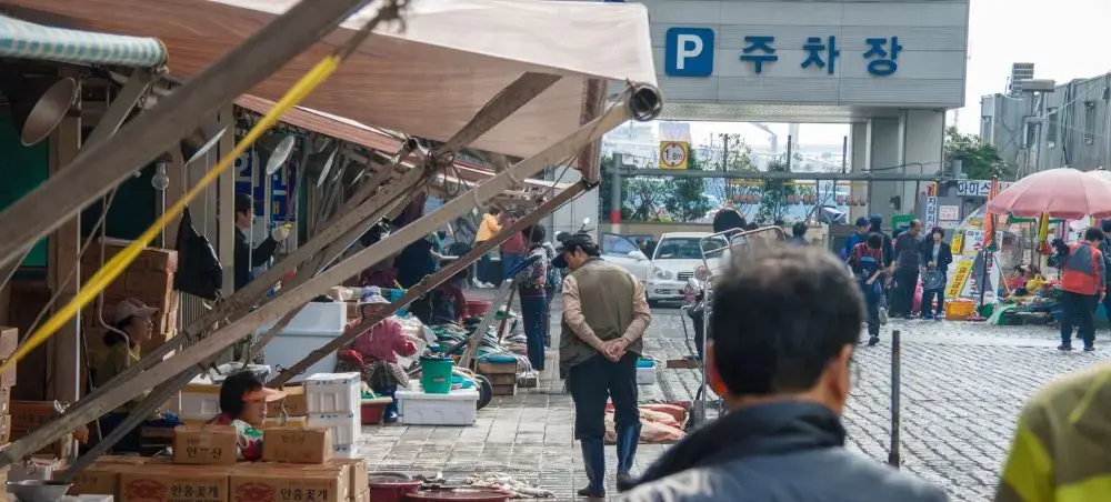 Bustling Busan fish market with vendors and shoppers beneath covered stalls near parking area