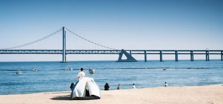 Gwangan Bridge spans across Busan's coastline with beachgoers enjoying the sandy shore and calm waters