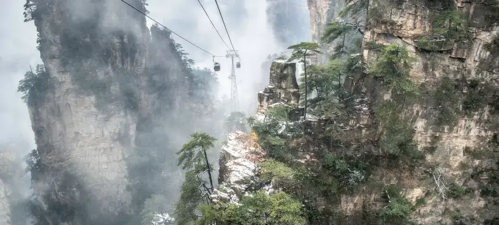 Cable car ascending through misty sandstone pillars and lush vegetation in China's dramatic mountain landscape