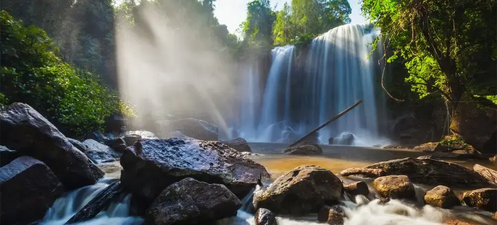 Pristine waterfall cascading through lush Cambodian jungle with golden sunlight filtering through tropical canopy