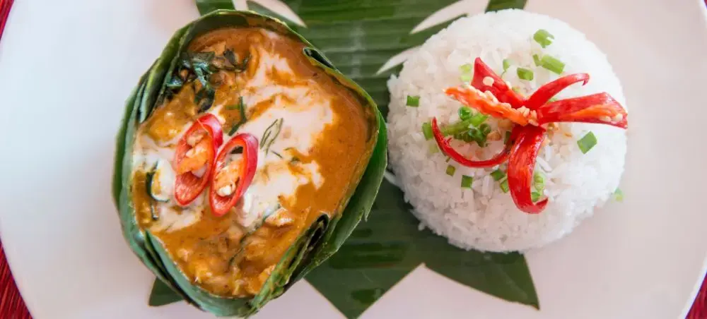 Traditional Cambodian fish amok curry served in banana leaf with jasmine rice and chili garnish