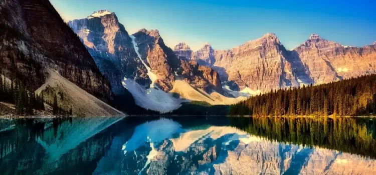 Pristine Canadian mountain lake reflecting snow-capped peaks and evergreen forests at golden hour
