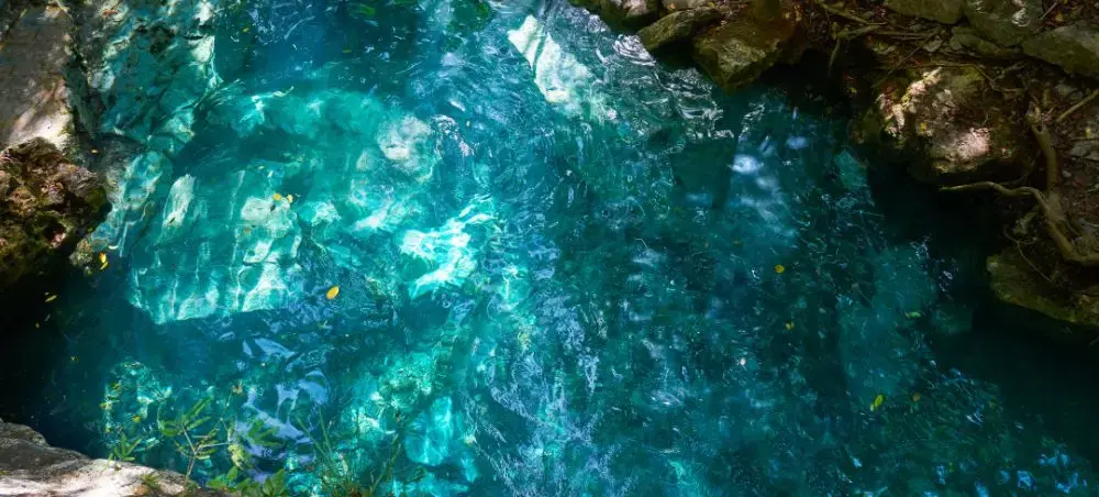 Crystal-clear turquoise cenote waters surrounded by ancient limestone rocks in Cancun's Yucatan Peninsula