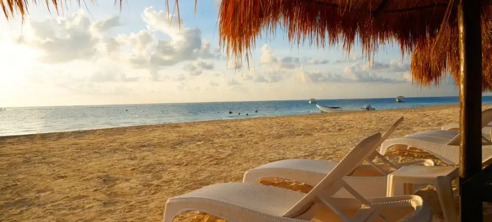 Luxury beach loungers under palapa shade overlooking pristine Cancun coastline at golden hour