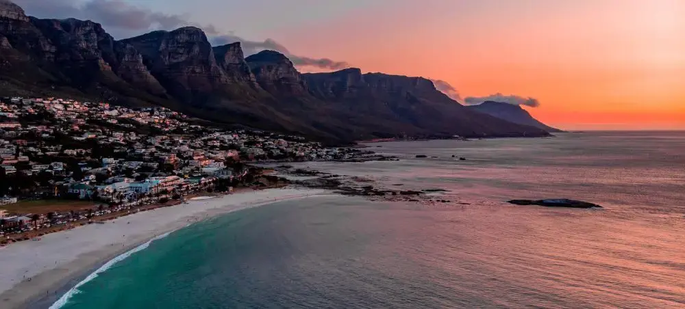 Dramatic sunset over Cape Town's Camps Bay beach with Twelve Apostles mountain range and luxury coastal homes