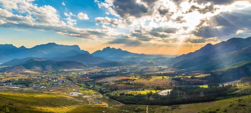 Panoramic view of Cape Town valley surrounded by dramatic mountain ranges under golden sunset sky