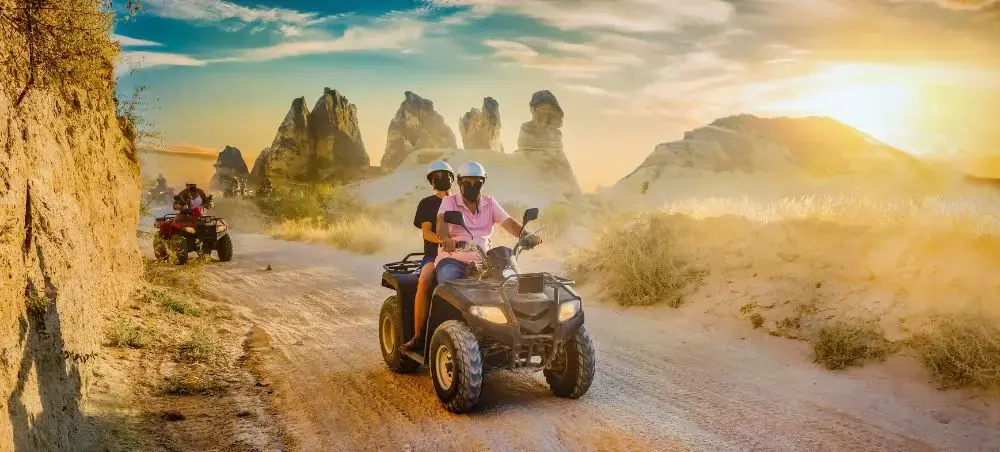 Couple enjoying ATV adventure through Cappadocia's iconic fairy chimneys and volcanic landscape at sunset