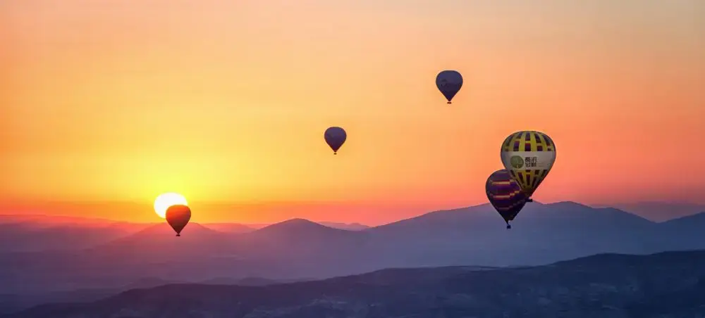 Hot air balloons floating over Cappadocia's layered mountains during golden sunrise in Turkey