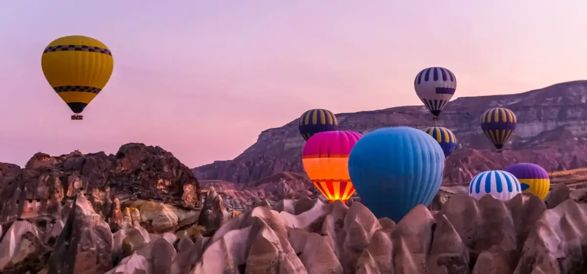 Colorful hot air balloons floating over Cappadocia's unique rock formations during golden hour sunrise