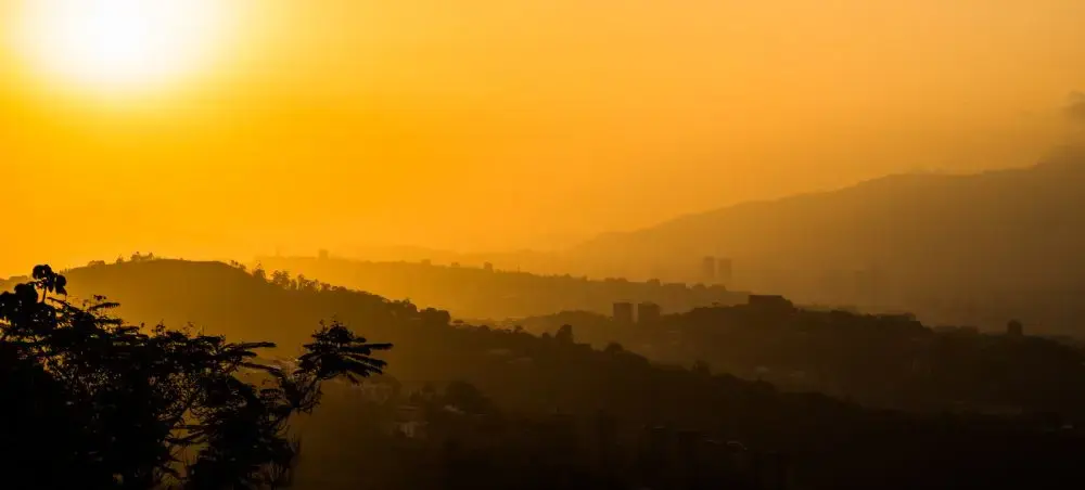 Golden sunrise illuminating Caracas valley with layered mountains and urban silhouettes in warm morning light
