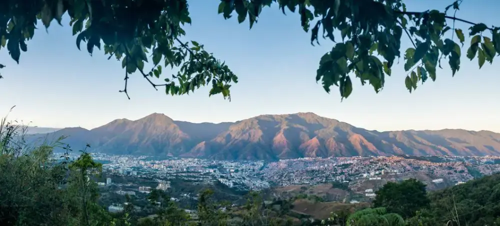 Panoramic view of Caracas cityscape nestled in valley with dramatic mountains under golden sunset light