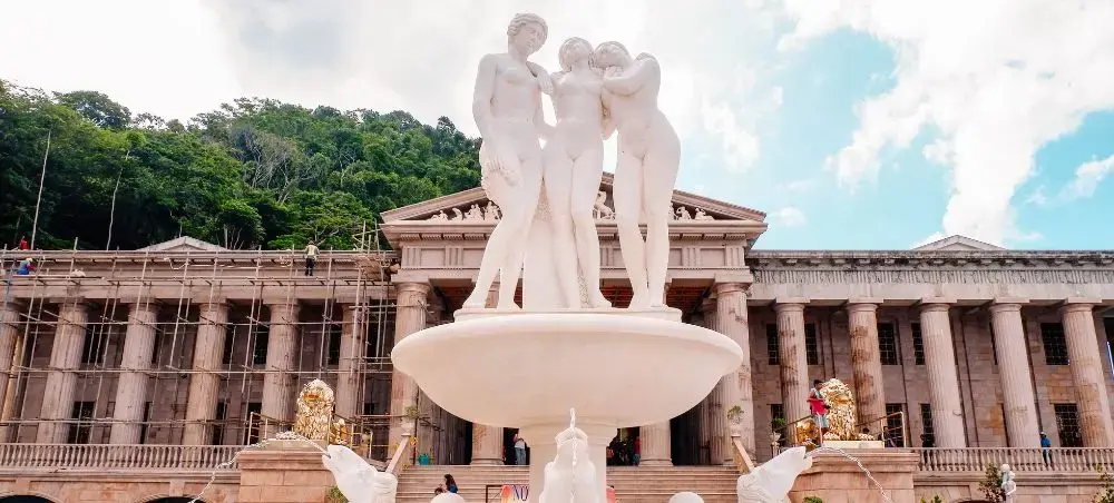 Classical white marble fountain with three figures stands before neoclassical government building in Cebu City