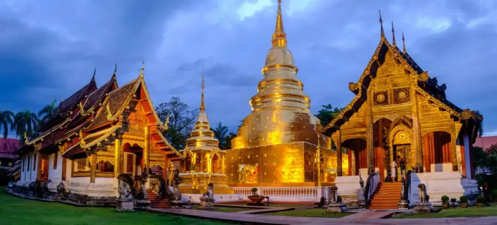 Golden illuminated Buddhist temple complex with traditional Thai architecture in Chiang Mai at twilight