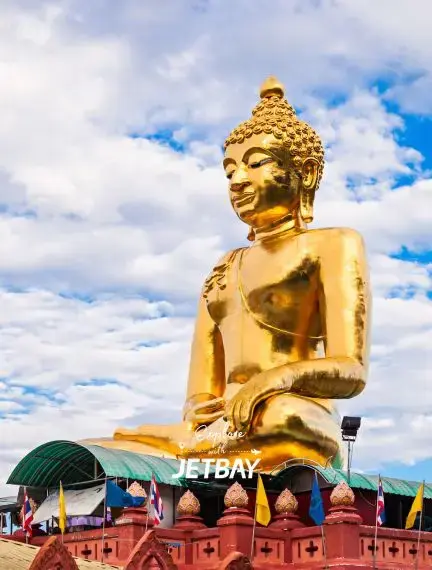 Golden Buddha statue towering over Chiang Rai temple complex under dramatic cloudy skies in northern Thailand