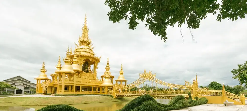 Golden ornate temple complex with traditional Thai architecture and decorative bridge in Chiang Rai