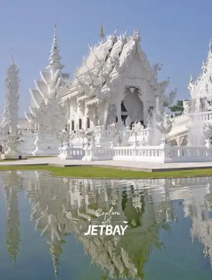 Wat Rong Khun White Temple in Chiang Rai reflecting in ornamental pond under clear blue sky