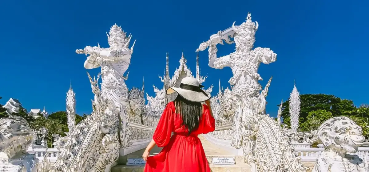 Woman in red dress exploring ornate white temple sculptures at Wat Rong Khun in Chiang Rai, Thailand