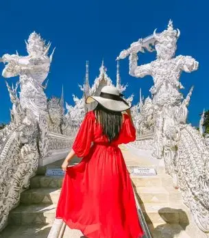 Woman in flowing red dress exploring ornate white temple sculptures in Chiang Rai, Thailand