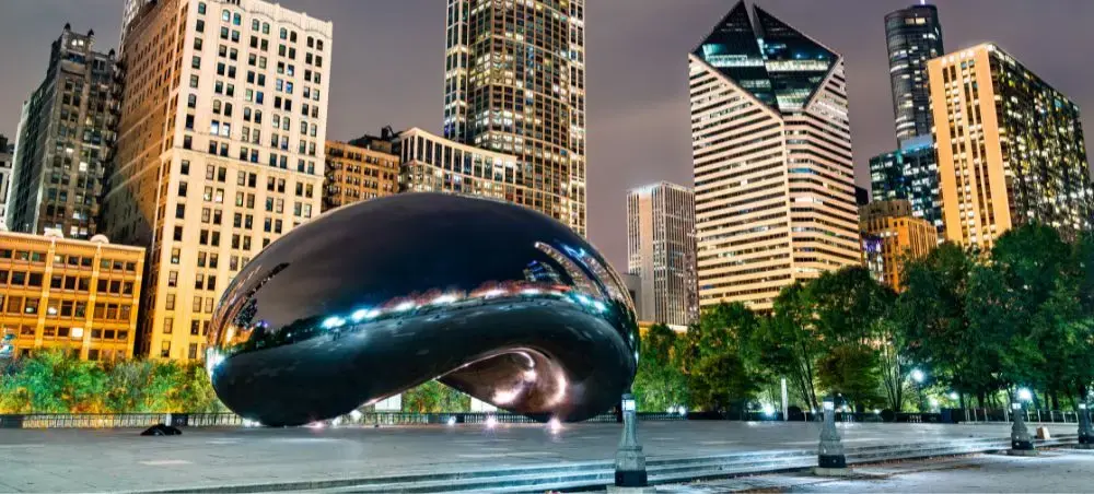 Chicago's iconic Cloud Gate sculpture reflects the illuminated downtown skyline at twilight in Millennium Park