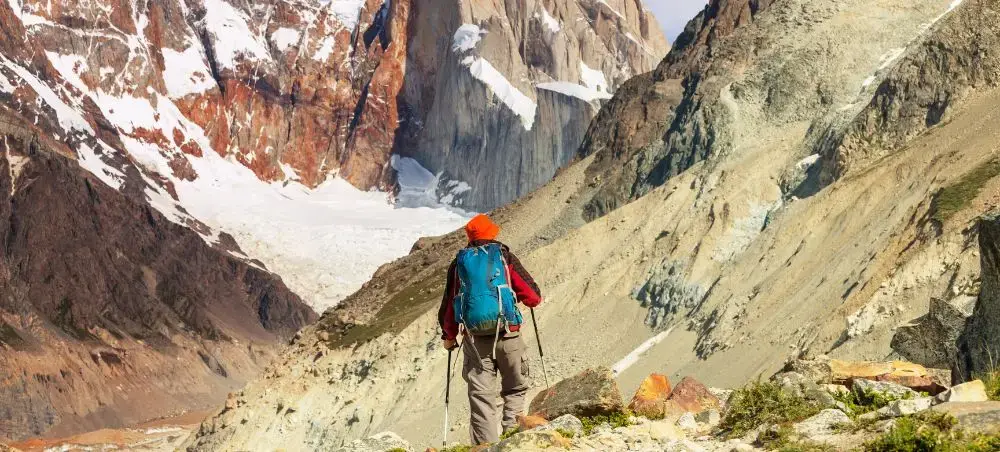 Mountaineer trekking through dramatic Chilean Andes canyon with snow-capped peaks and rugged terrain