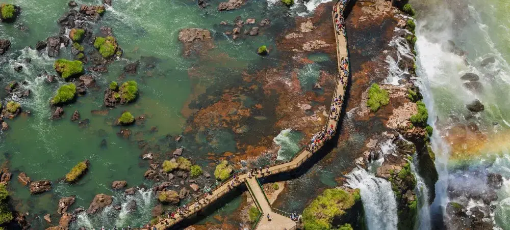 Aerial view of wooden walkways crossing turquoise waters near Iguazu Falls with visitors exploring the scenic boardwalks