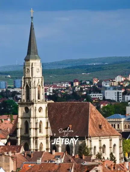 Gothic church spire dominates Cluj-Napoca cityscape with red-tiled roofs and rolling hills beyond